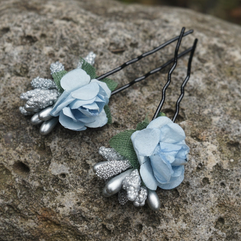 Two floral hair pins with blue flowers and silver accents on a light gray background