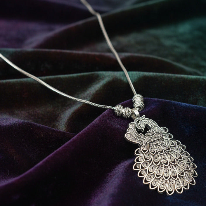 Silver peacock-shaped pendant on a chain against a dark fabric background