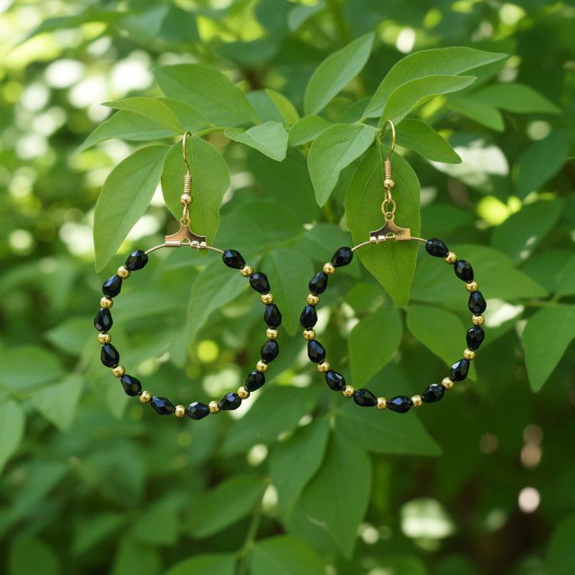 Pair of black beaded earrings with gold accents on a gray background