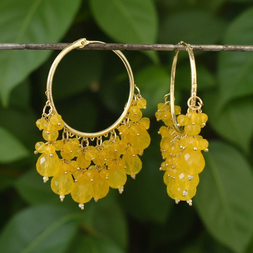 A pair of gold-colored hoop earrings with yellow dangling beads and small clear accents