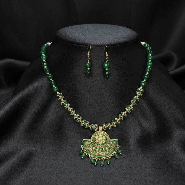 Traditional green and gold necklace with matching earrings on a dark fabric background