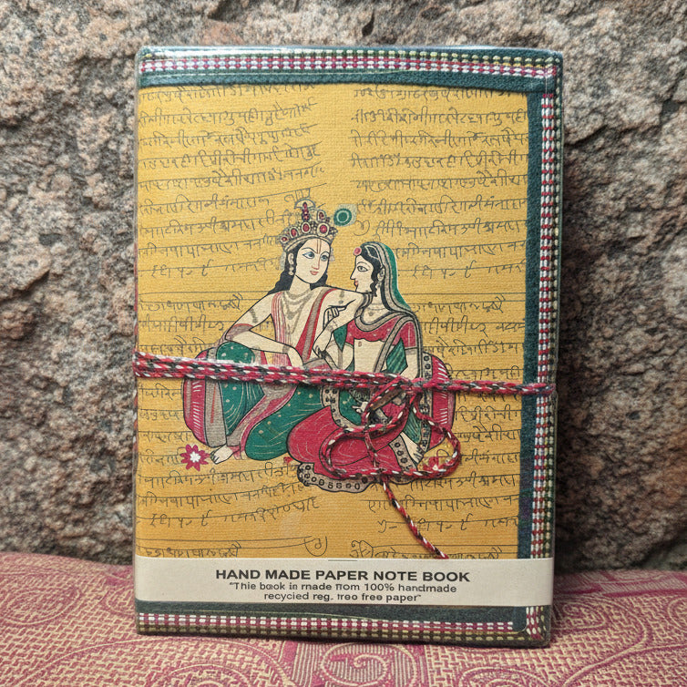 Notebook with decorative cover featuring two women and text, placed on a patterned fabric background.